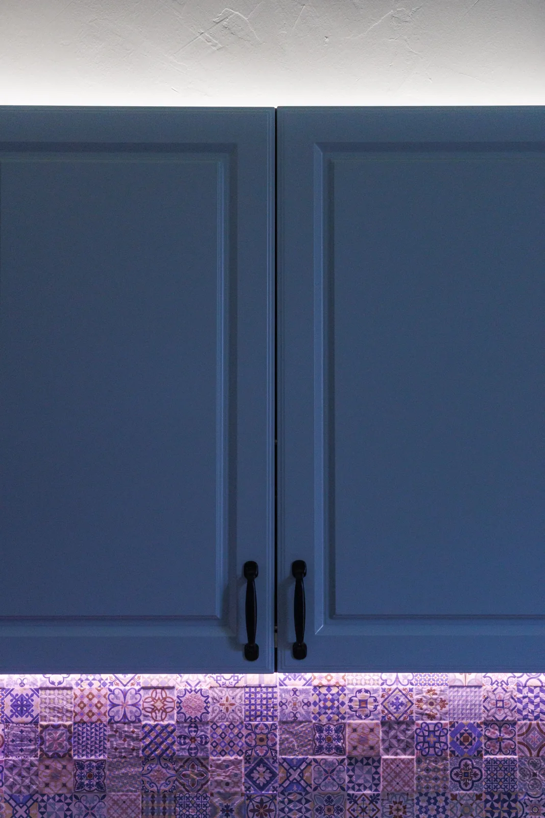 Blue painted cabinet doors above a patterned tile backsplash