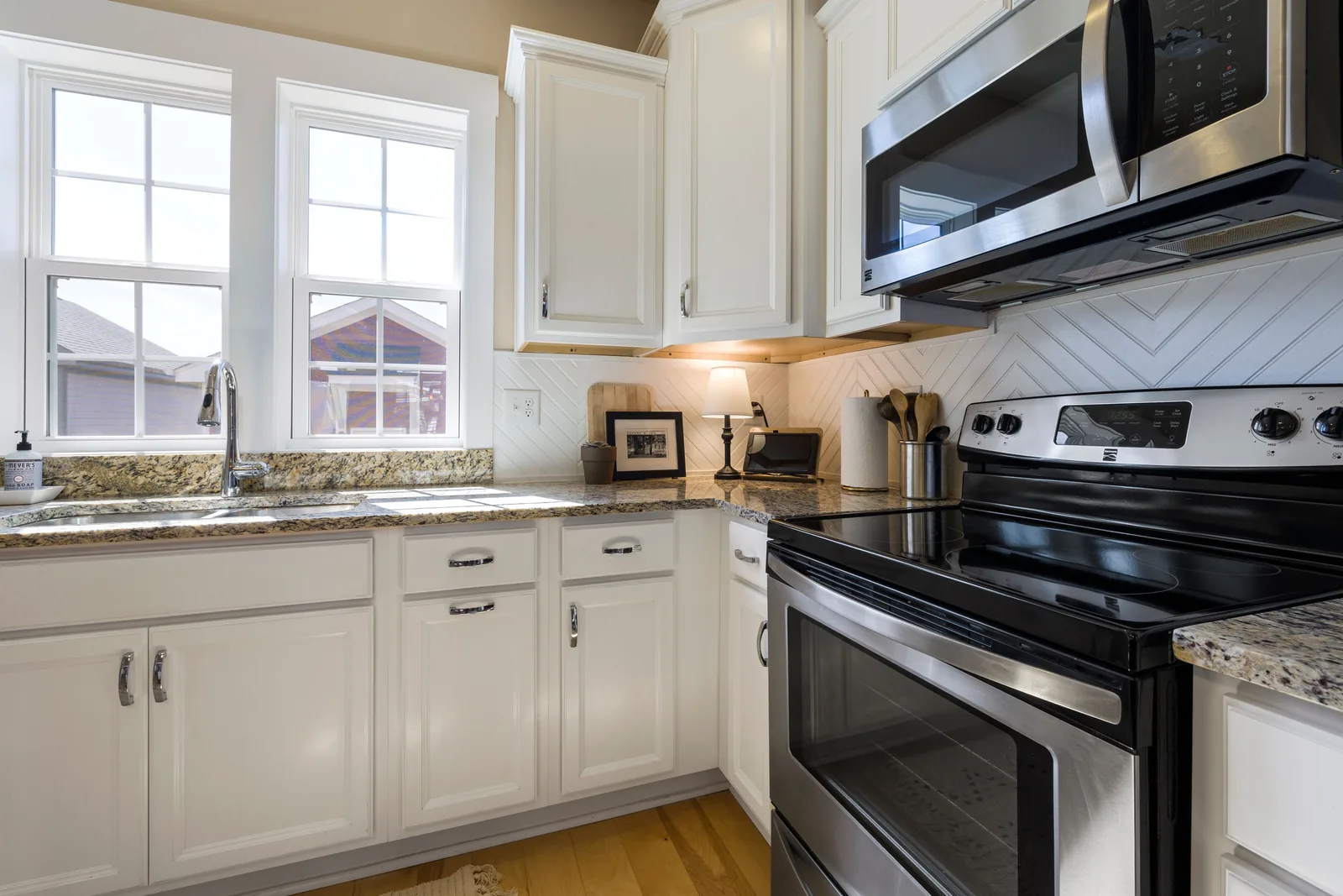 White cabinets with a granite worktop and chevron tile backsplash