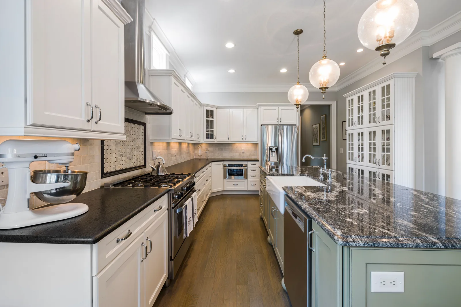 A white raised-panel kitchen with a green island and farmhouse sink